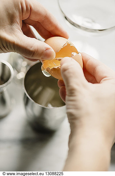 Cropped image of woman breaking egg in drinking glass