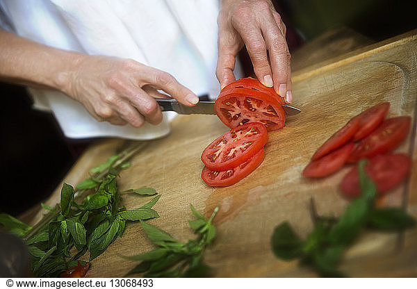 Cropped image of woman cutting tomato slices by mint leaves on cutting board