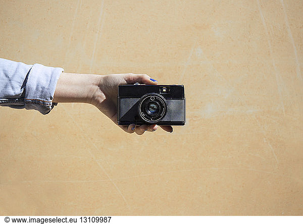 Cropped image of woman holding camera against wall