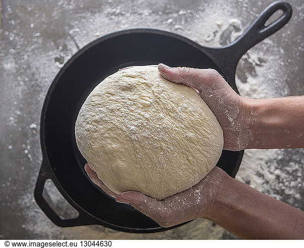 Cropped image of woman holding dough over cooking pan in kitchen
