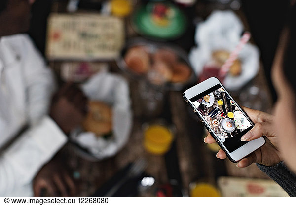 Cropped image of woman photographing food on dining table at restaurant