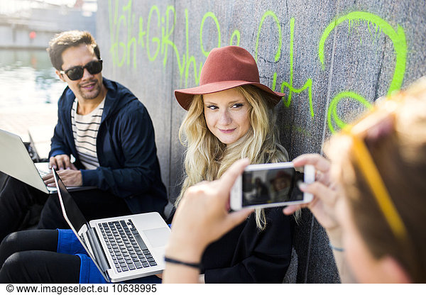 Cropped image of woman photographing freelancers sitting against wall