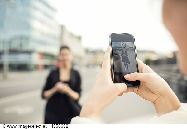 Cropped image of woman photographing friend in city