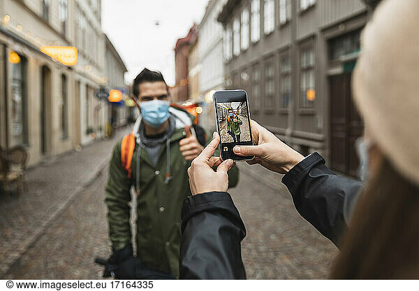 Cropped image of woman photographing man through smart phone during pandemic