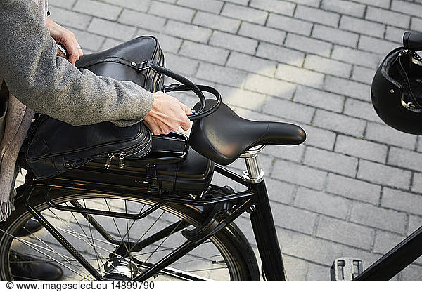 Cropped image of woman positioning bag on electric bicycle in city