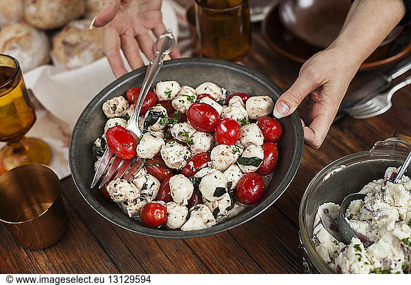 Cropped image of woman serving tomato and cottage cheese salad at table