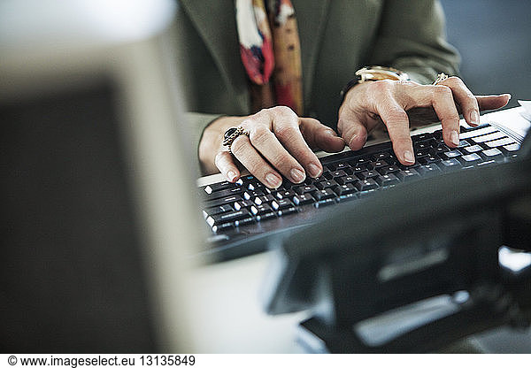 Cropped image of woman typing on computer keyboard at office desk