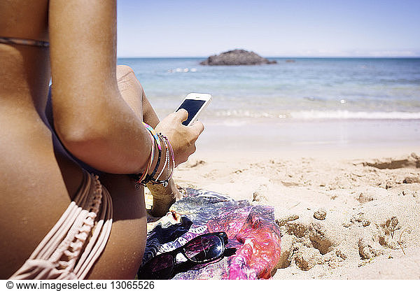 Cropped image of woman using phone while sitting at shore