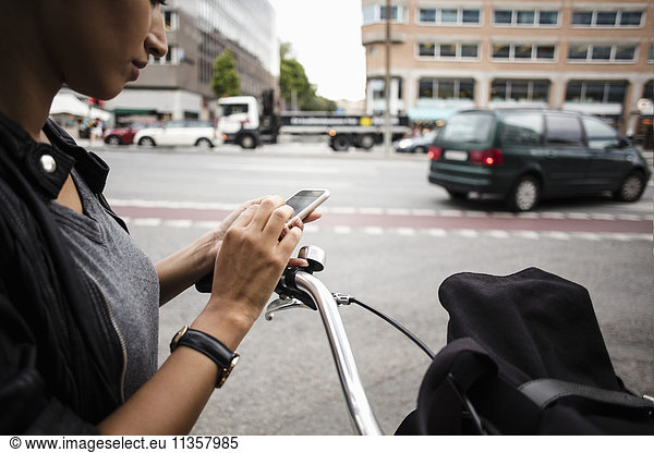 Cropped image of woman with bicycle using mobile phone while standing by street in city