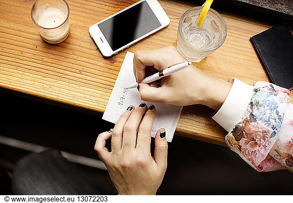 Cropped image of woman writing on tissue paper while sitting in bar