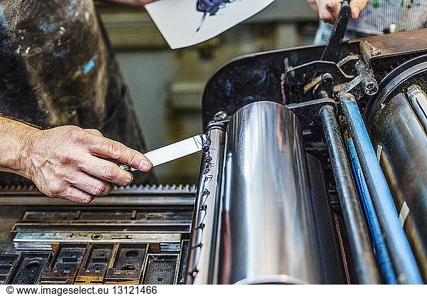 Cropped image of worker applying blue ink on printing roller at workshop