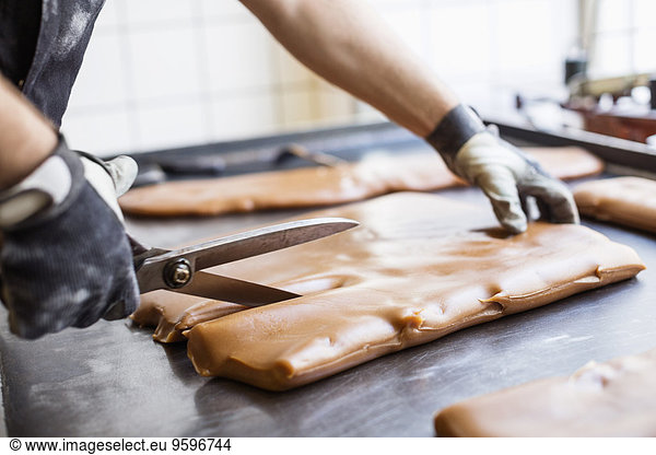 Cropped image of worker cutting caramel with scissors in candy store