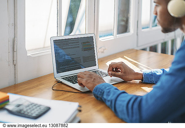 Cropped image of young man blogging through laptop computer at table by window