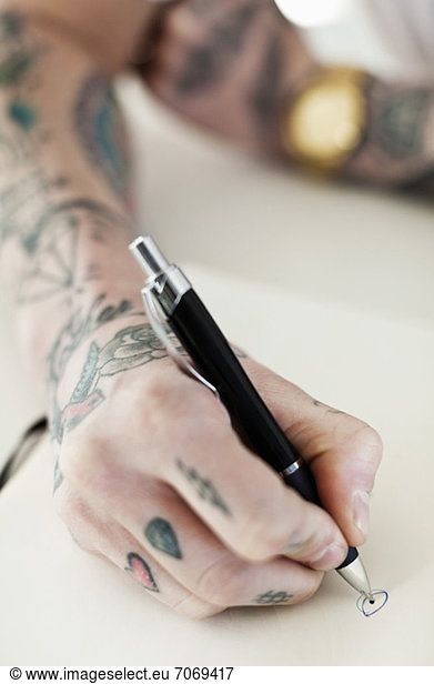 Cropped shot of a tattooed hand writing