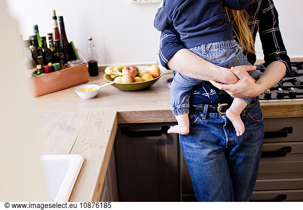 Cropped shot of mid adult woman carrying baby son in kitchen
