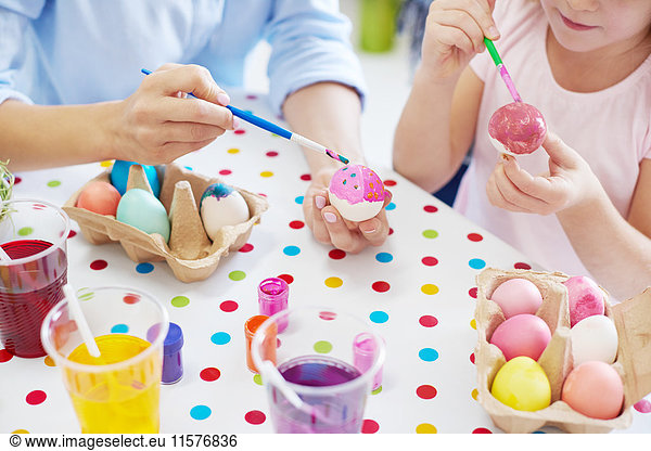 Cropped shot of woman and daughter's hands painting easter eggs at table
