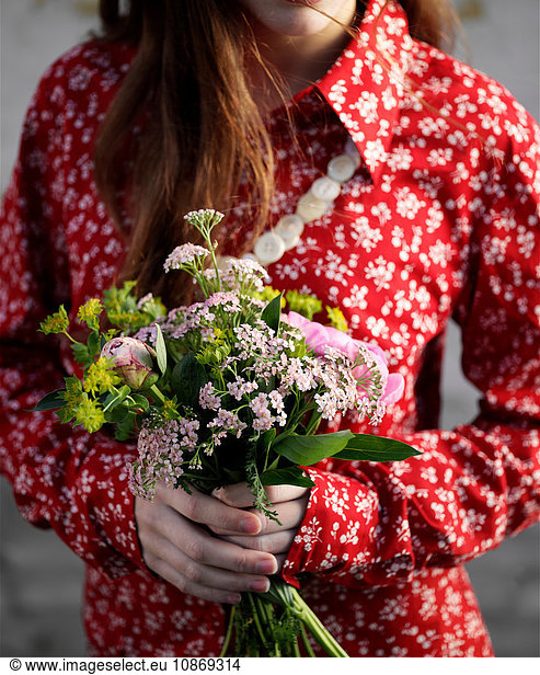 Cropped shot of woman wearing red floral blouse holding bunch of flowers