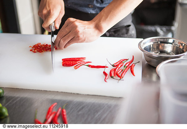 Cropped view of man slicing red chilli peppers
