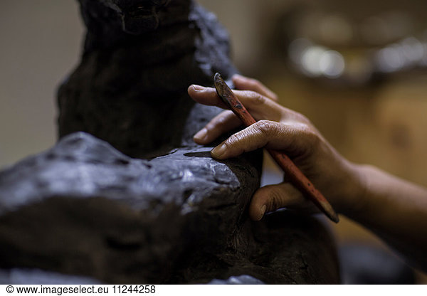 Cropped view of sculptor in artists' studio creating sculpture with hand tool