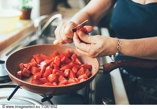 Cropped view of woman chopping tomatoes into saucepan