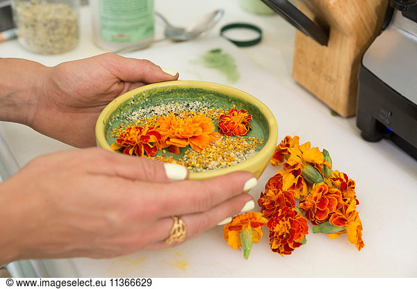 Cropped view of woman's hands holding bowl of food garnished with flowers