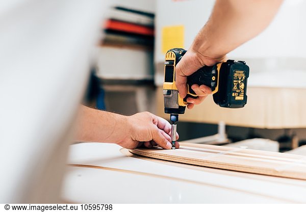 Cropped view of young man in carpentry workshop using cordless screwdriver  screwing into plywood