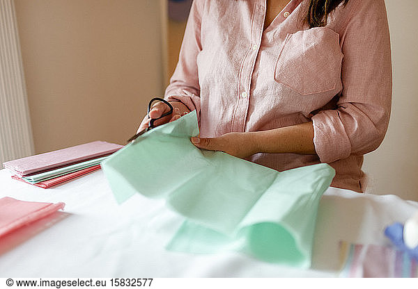 Cropped woman cutting green tissue paper during tutorial