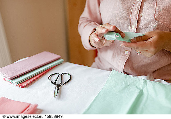 Cropped woman cutting green tissue paper during tutorial workshop