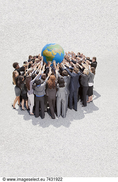 Crowd of business people in huddle lifting globe overhead