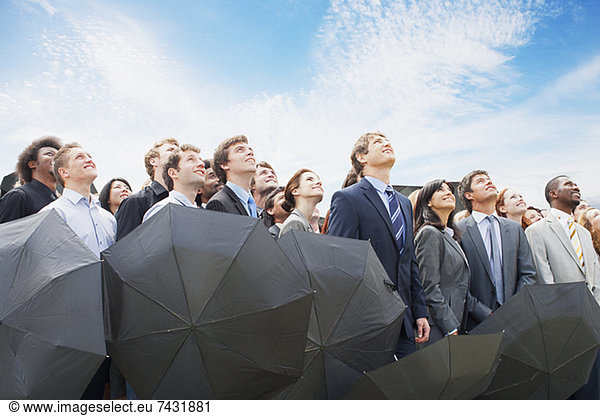 Crowd of business people with umbrellas looking up at sky