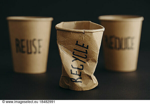 Crushed reusable cup with recycle text written on it against black background