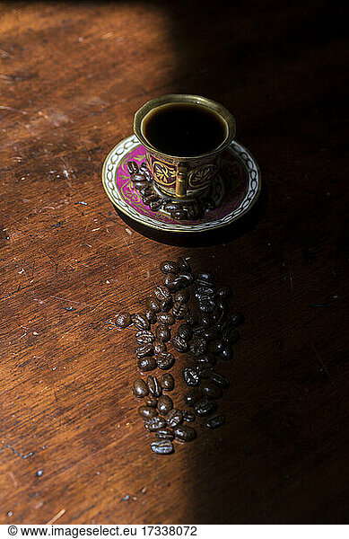 Cup of coffee and raw coffee beans lying on shaded table