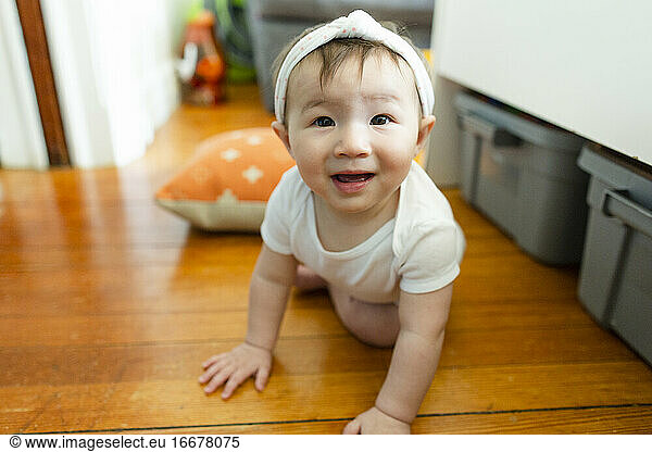 Curious baby girl makes eye contact while crawling on floor at home