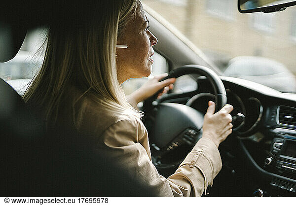 Curious businesswoman with in-ear headphones driving car