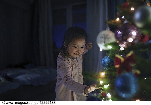 Curious  cute girl touching illuminated Christmas tree