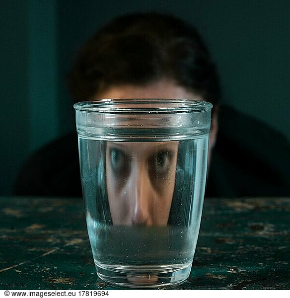 Curious face of a woman reflected in a water glass