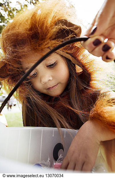 Curious girl in Halloween costumes removing candy from bucket during trick or treating