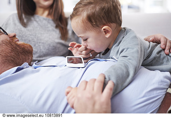Curious toddler looking at cell phone on father’s chest