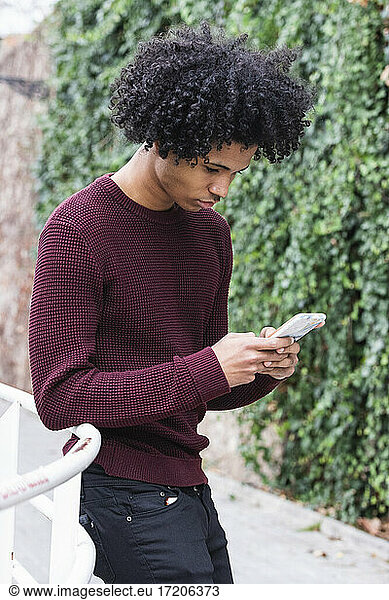 Curly hair boy using mobile phone while standing by railing