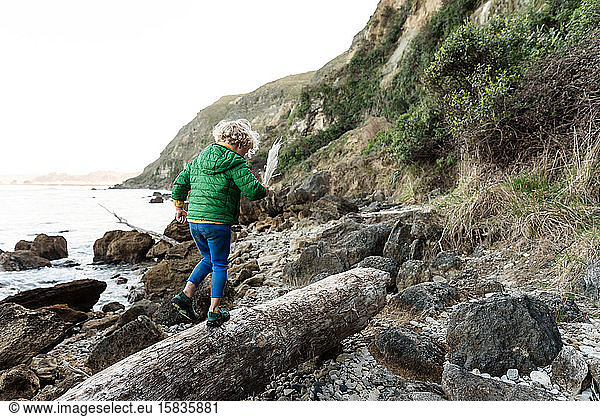 Curly haired child walking on log near ocean in New Zealand