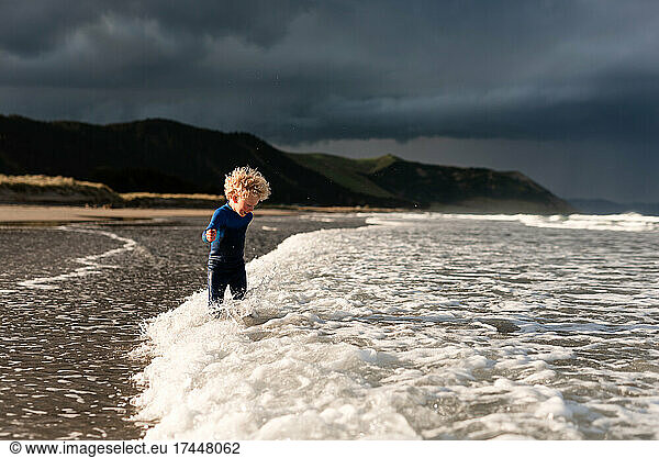 Curly haired kid playing in waves at beach in New Zealand