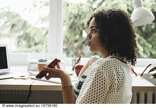 Curly haired teenage girl talking on smart phone at desk near window