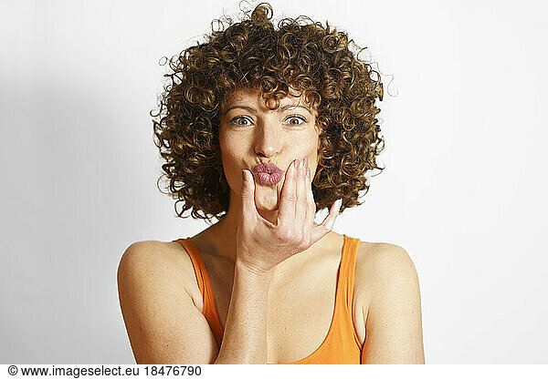 Curly haired woman puckering face against white background