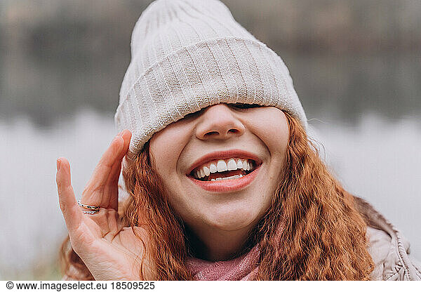 Curly redhead woman 30-35 with a cap over her eyes laughs