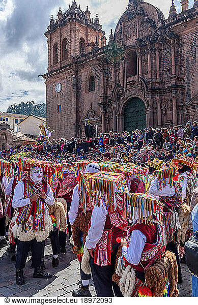 Cusco  a cultural fiesta  people dressed in traditional colourful costumes with masks and hats  brightly coloured streamers  in the Cusco central square by the cathedral.