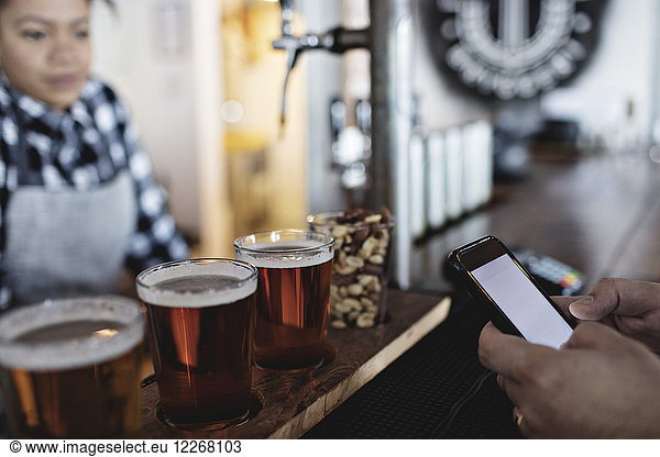 Customer doing contactless payment through smart phone to female bartender for beer at counter