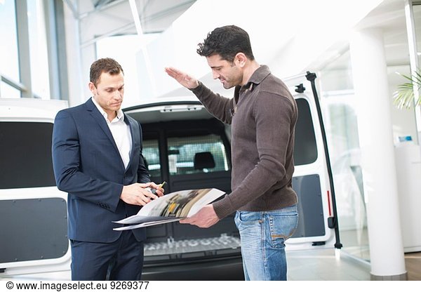 Customer questioning salesman in car dealership