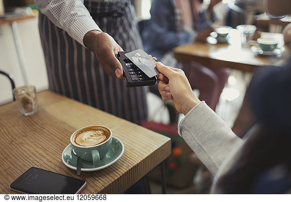 Customer with credit card paying worker with contactless payment in cafe