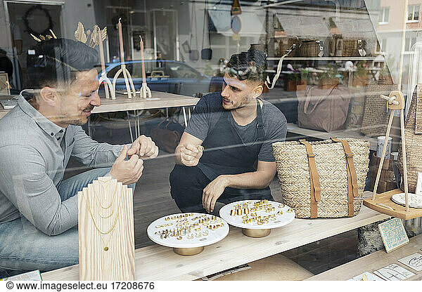 Customer with male entrepreneur trying rings seen through glass of design studio