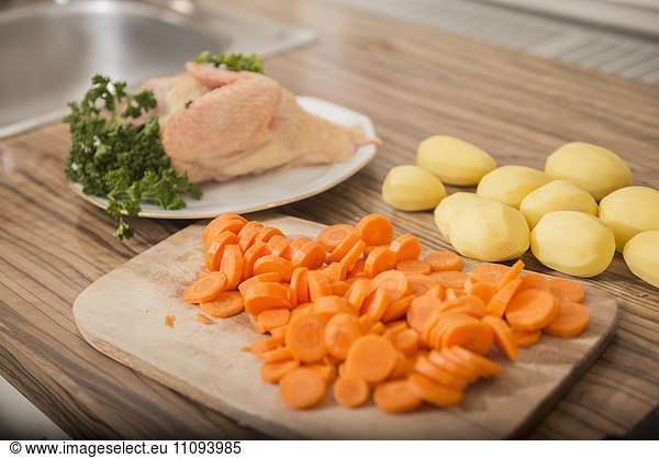 Cut carrots  peeled potatoes  raw chicken with parsley at kitchen counter